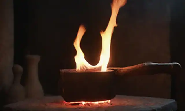 Un herrero forja con un martillo en forma de mango de madera que se inclina contra el yunque
