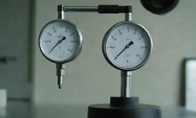 Un dispositivo mecánico con un brazo cargado de resorte, un medidor de esfera o pantalla digital, y un peso o objeto que se levanta, un manómetro o un medidor de presión en el fondo, un laboratorio científico o un taller