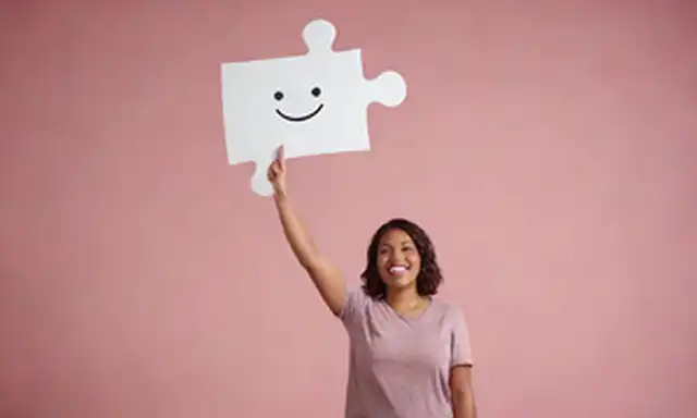 ilustración 3D de una persona de pie frente a una pieza de rompecabezas gigante, con las manos sostenidas y palma hacia arriba, rodeada de burbujas de discurso con caras sonrientes, en medio de un fondo sutil gradiente