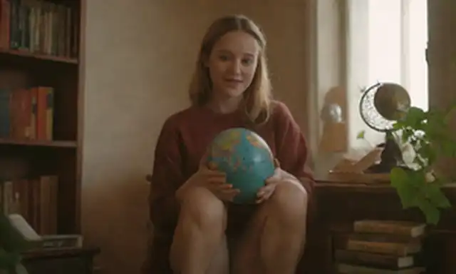 Una persona sentada en un taburete, con libros y herramientas alrededor de ellos; manos sosteniendo un globo, con hojas y flores brotando de él; ojos mirando hacia arriba, rodeado de luz suave; una sonrisa sutil; gesto suave de apertura; un sentido de armonía entre los mundos interior y exterior