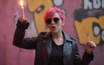 Una persona joven con pelo rosa brillante usando una chaqueta de cuero y gafas de sol