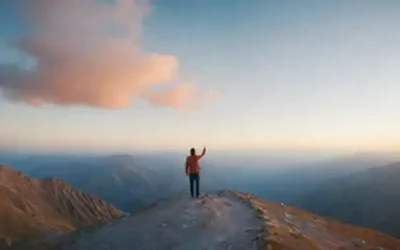 Una persona de pie en un pico de montaña con una mano levantada