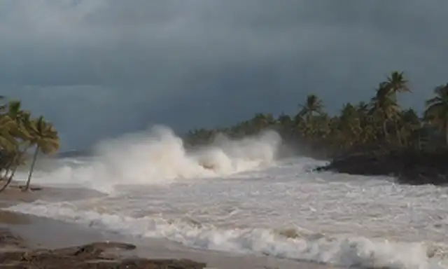 olas chocando en la orilla, edificios destruidos, escombros esparcidos, gente corriendo en pánico, botes volcados, palmeras desarraigadas, luz solar brillante que se desvanecen a nubes oscuras, espuma oceánica, caos y destrucción desplegadas, tsunamis furiosos desatado
