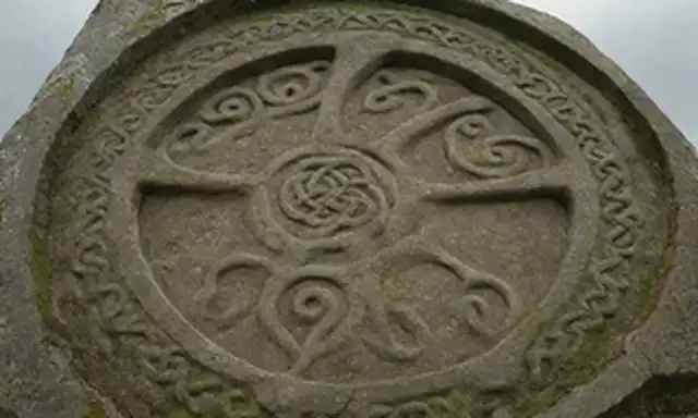 Un antiguo monumento celta, símbolo triskel grabado en piedra, líneas en espiral que se curvan hacia fuera, cuernos o antlers formando el eje central, nudos intrincados adornan las superficies circundantes, climatizado a una pátina mosy